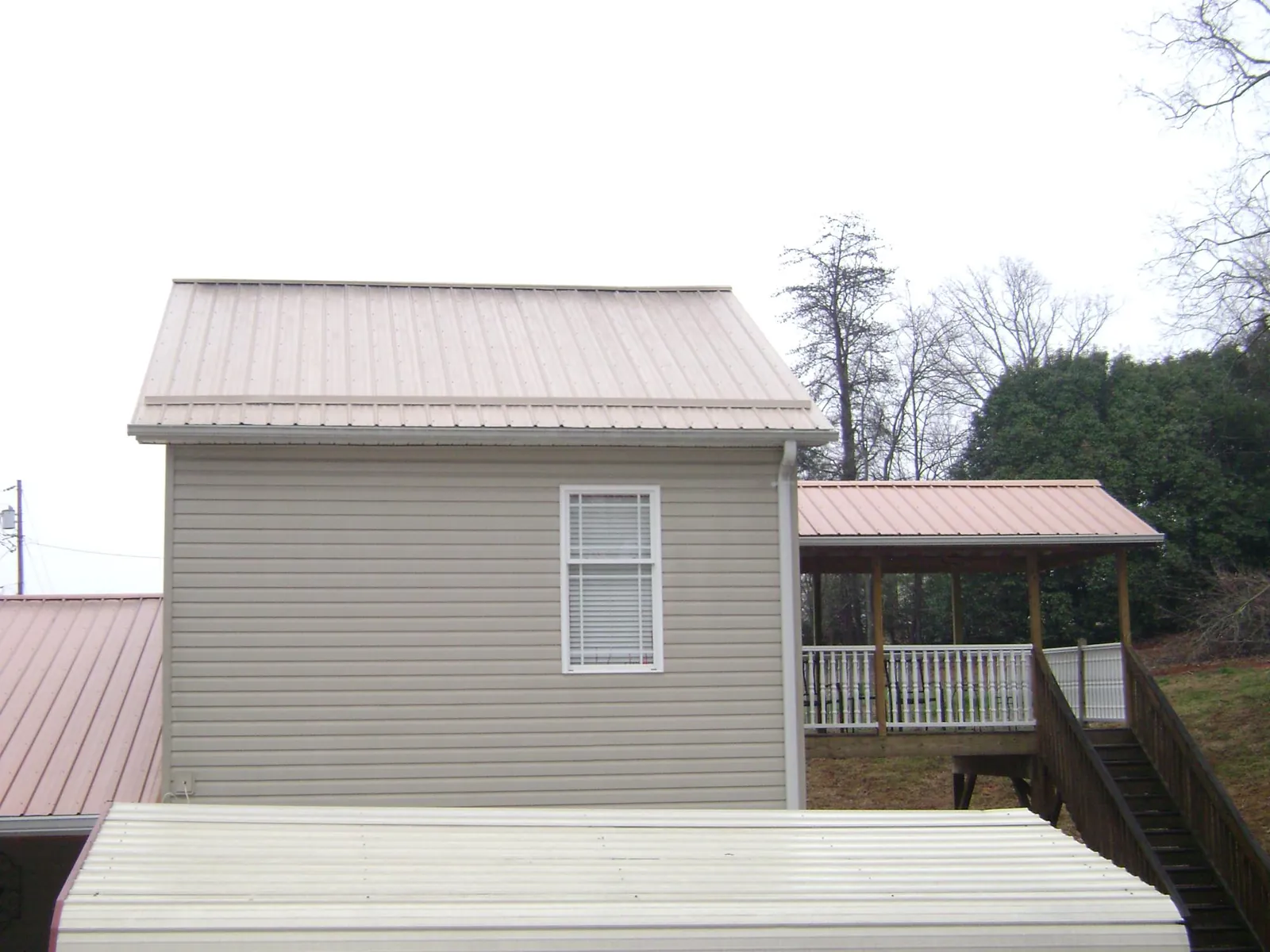 Tan metal roofs on a two story addition and attached porch, from a Roof Replacement job in Hayward